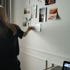 Woman arranging photos on wall in modern office, laptop on desk, creative workflow.