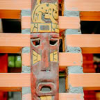 Decorative wooden tribal mask on orange brick wall outdoors.