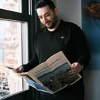 Man standing by window reading a newspaper in Istanbul. Casual indoor setting.