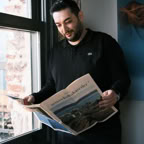 Man standing by window reading a newspaper in Istanbul. Casual indoor setting.